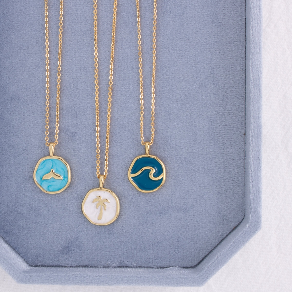 Three gold necklaces with unique pendants on a blue display box.