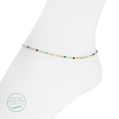 Gold anklet with blue beads on a white foot against a white background