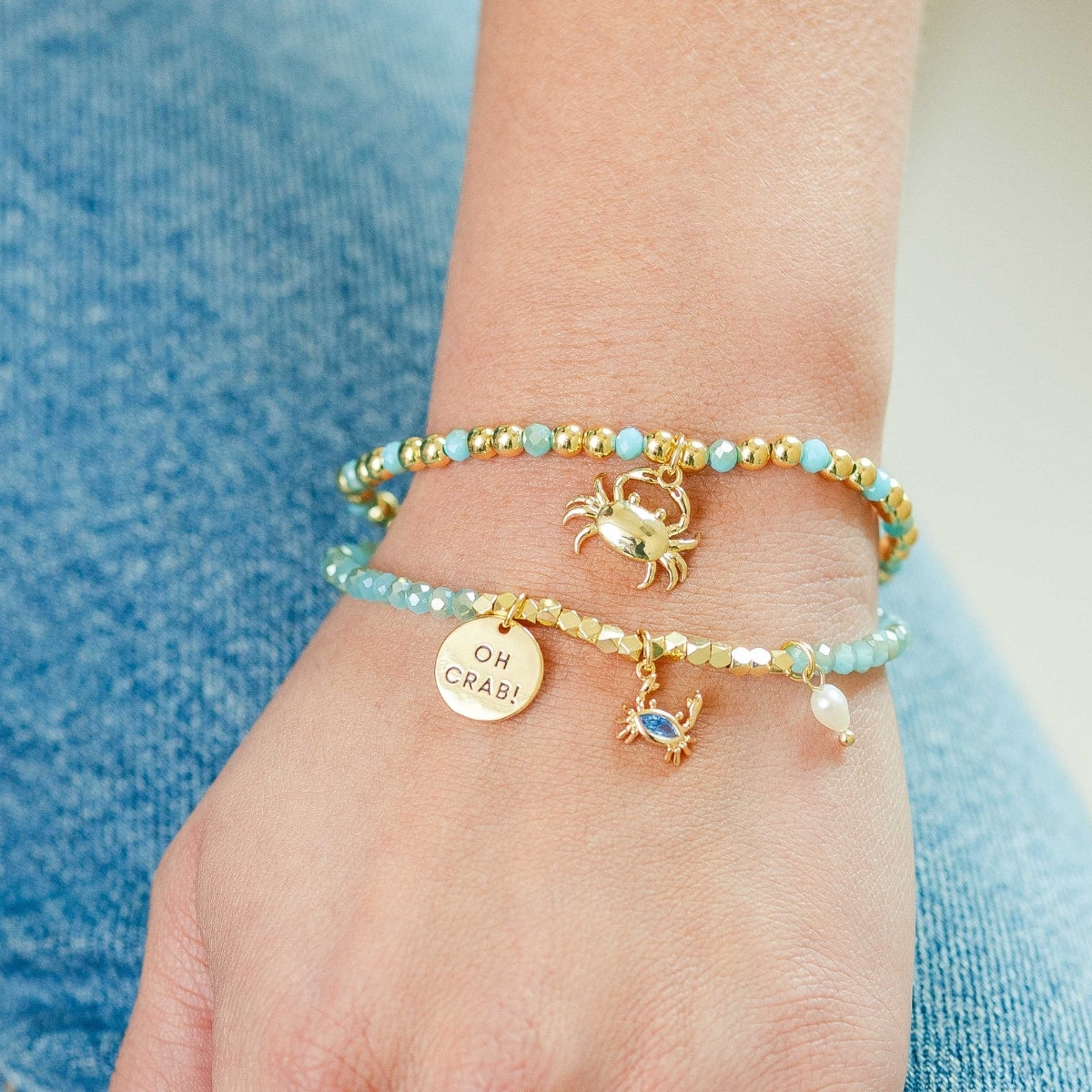 Bracelets with crab charms and gemstones on a wrist against a blue denim background