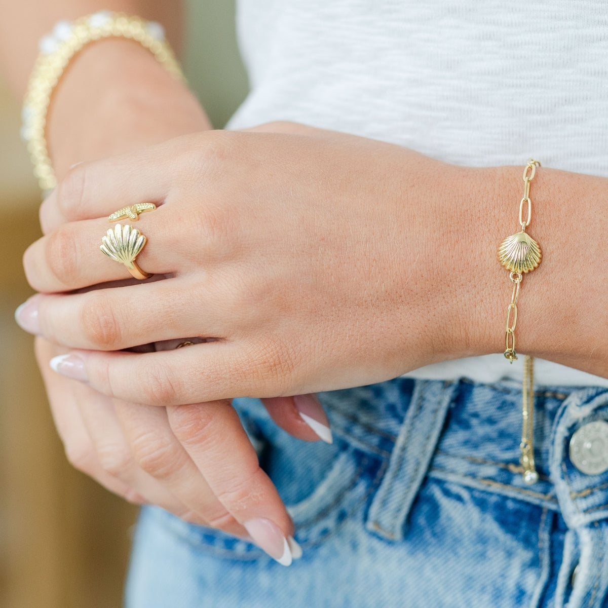 Close-up of a hand wearing gold shell ring and bracelet with denim jeans in the background