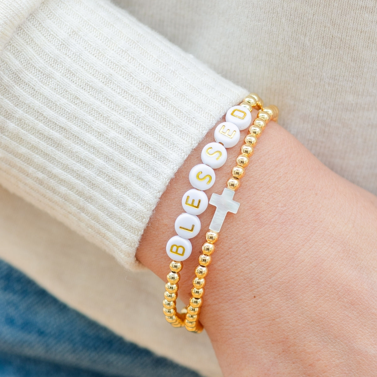 Gold bracelet with 'BLESSED' beads on a wrist against a neutral background