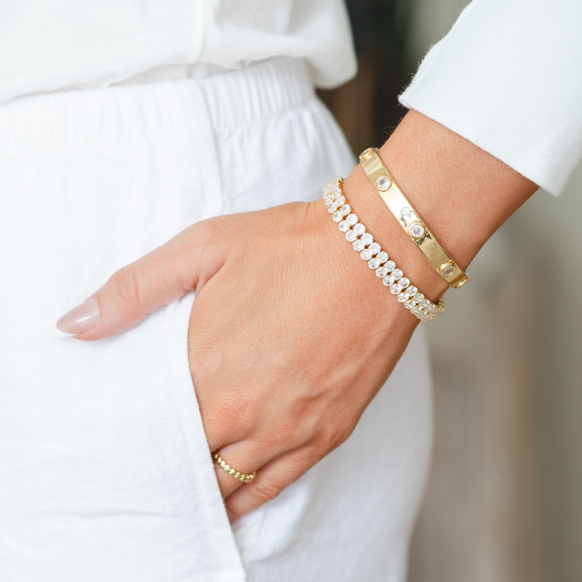 Hand wearing gold and pearl bracelets on a blurred white background