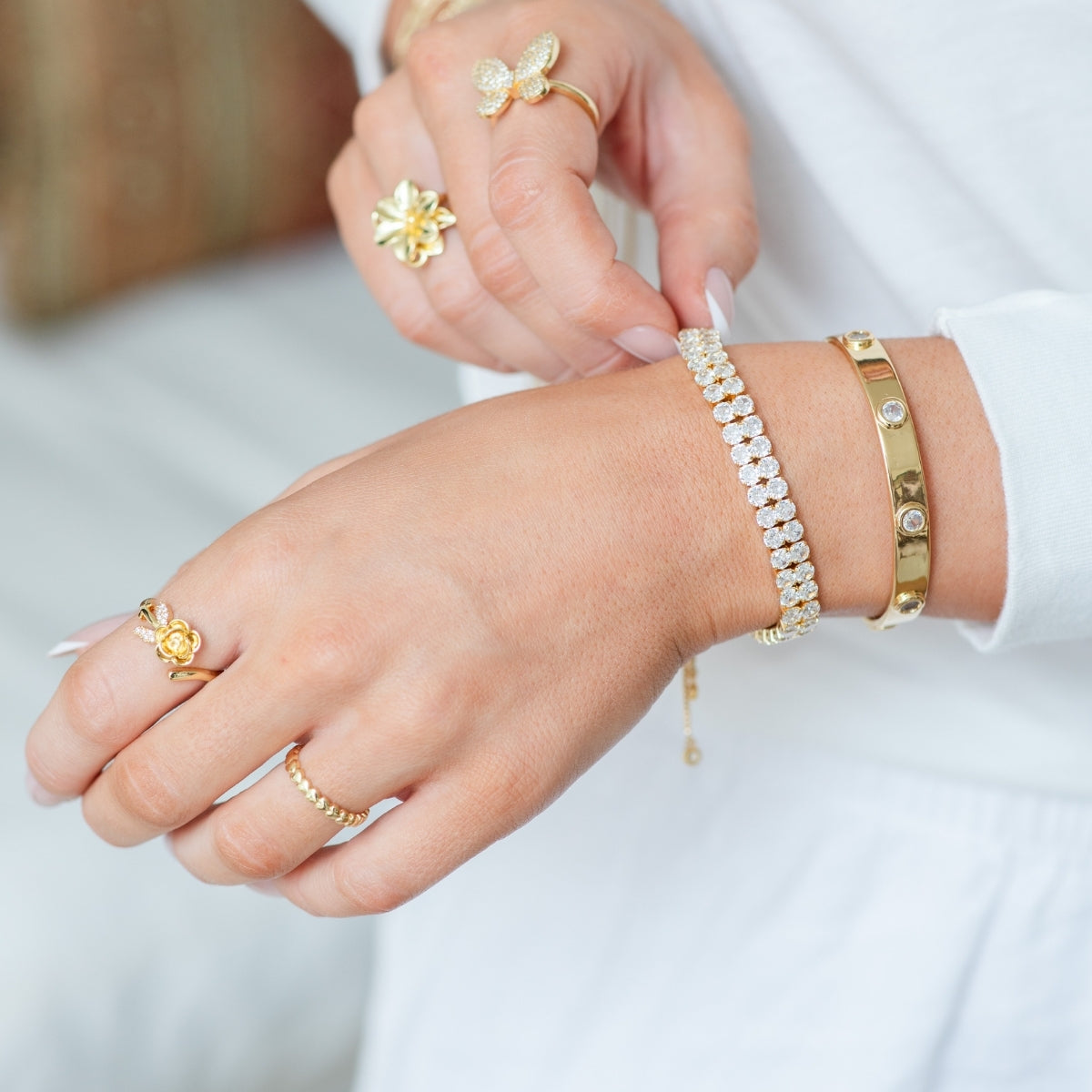 Close-up of a hand wearing gold and diamond bracelets and rings on a white background