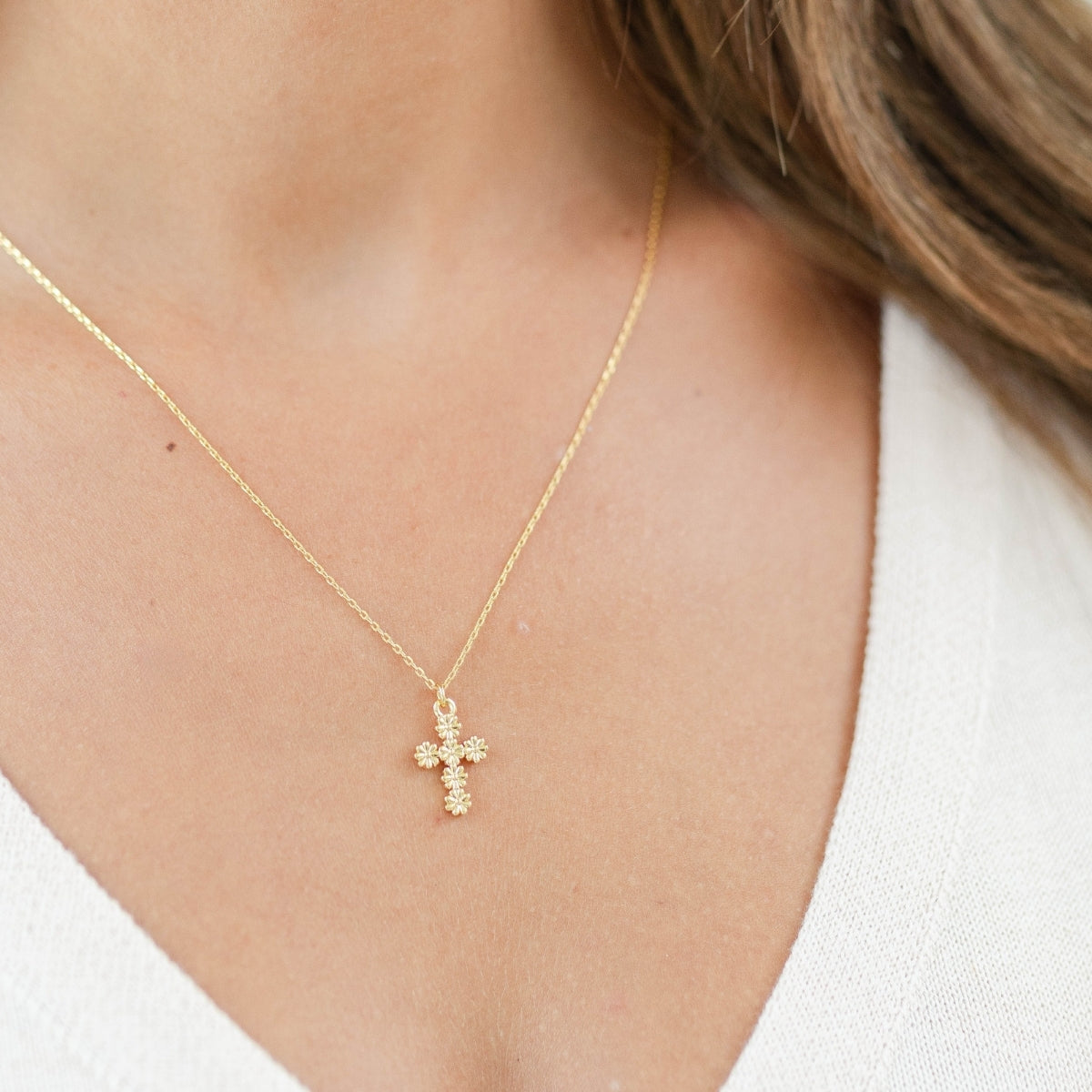 Gold cross necklace on a person wearing a white top