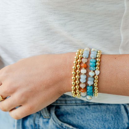 Close-up of a wrist wearing multiple beaded bracelets on a plain background