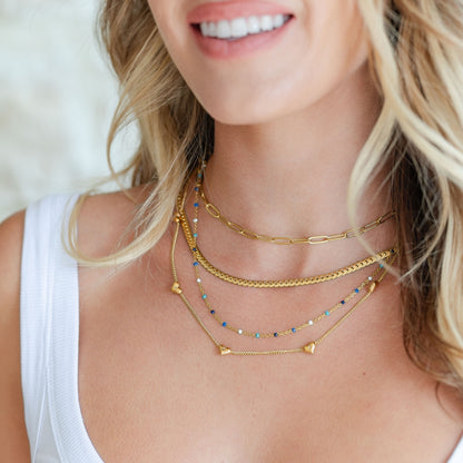 Woman wearing multiple gold necklaces with a blurred background